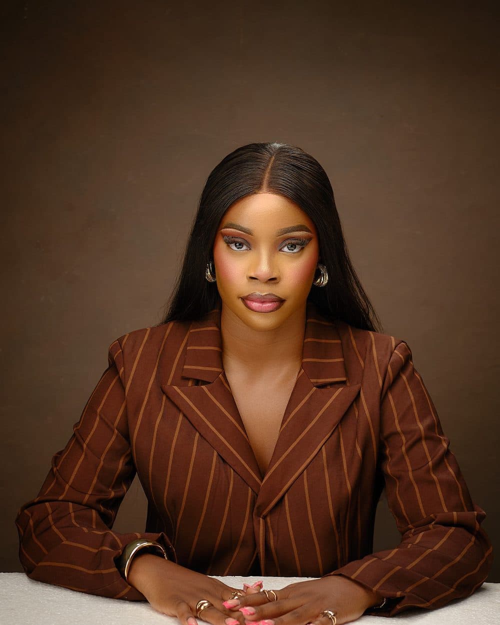 Achiever Omoobajesu in a brown pinstripe blazer, seated at a table with her hands clasped